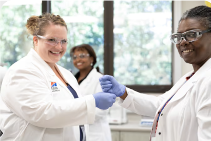 Zwei Wissenschaftler in Laborkitteln und Handschuhen lächeln und schütteln sich in einer Laborumgebung die Hände.
